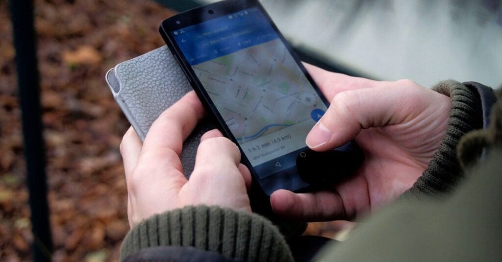 Person holding a smartphone showing a map navigation app outdoors, with a route visible on screen.